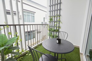 Ein Balkon mit rundem Tisch und Stühlen, einem Blumentopf und einer Rankgitter mit Kletterpflanzen.