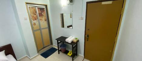 A hotel room with a bed, a desk, a chair, a door, and a window.