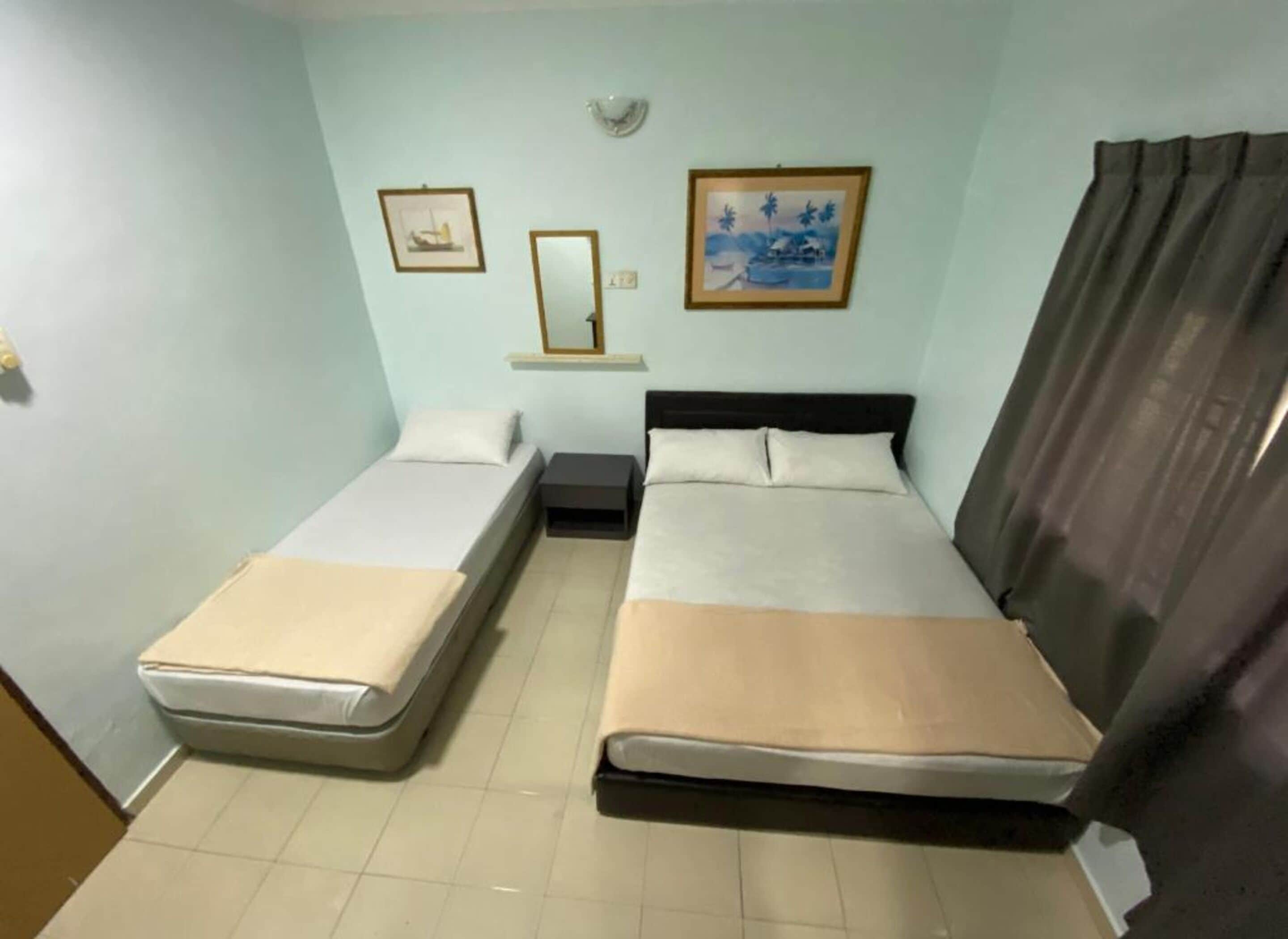 Een kleine, eenvoudige kamer met twee enkele bedden, een nachtkastje, een spiegel en twee ingelijste foto's aan de muur.