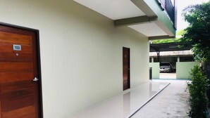 A hallway with a wooden door labeled '103', a small door, and a concrete floor leading to a covered area with a car parked outside. - B.O Best Residence (Phang Nga)