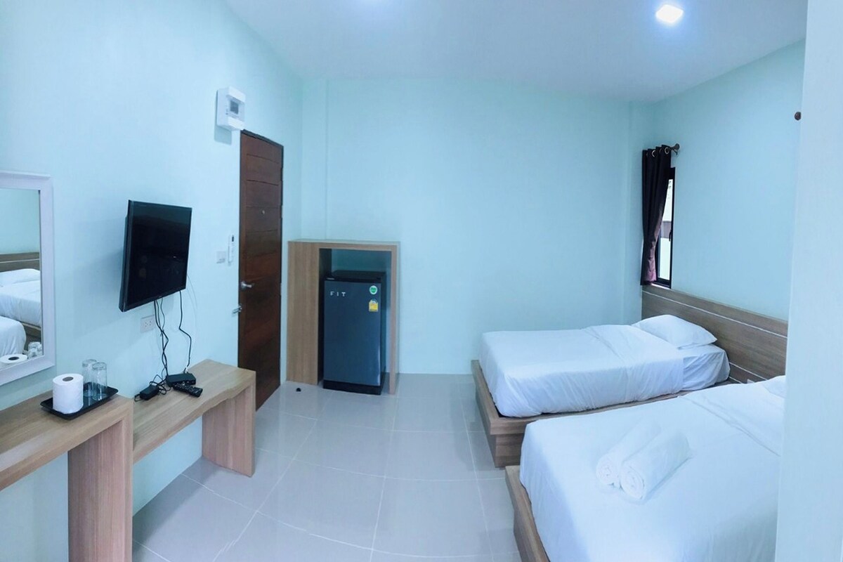 A hotel room with two beds, a TV, a desk with a computer, a small fridge, and a mirror.