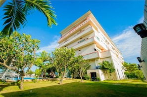 Un hotel de varios pisos con techo plano, rodeado de césped cuidado y palmeras.