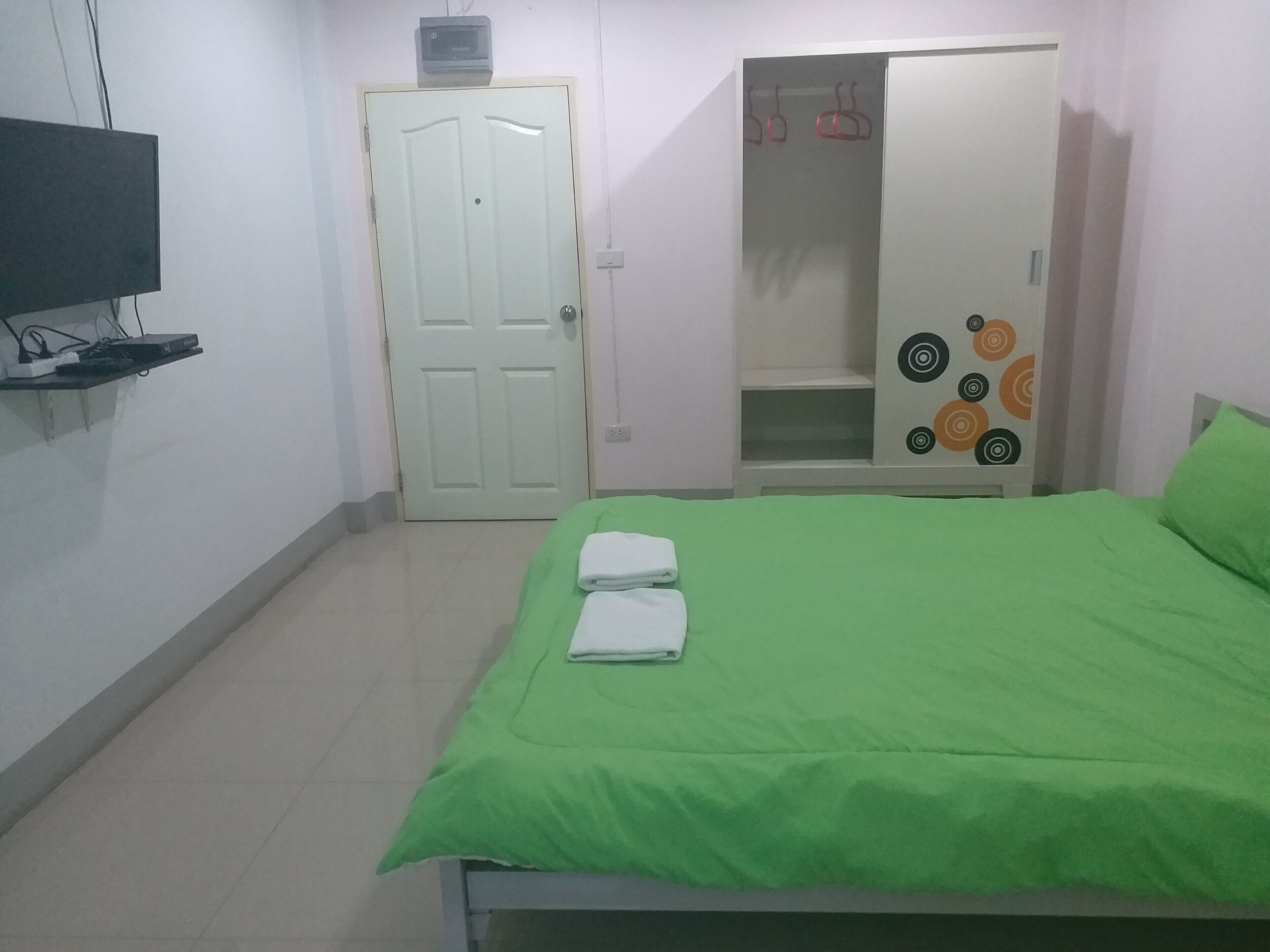 Een slaapkamer met een groene sprei, een witte deur, een garderobe met een rond ontwerp en een plank met elektronische apparaten.