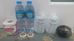 Una mesa con artículos de tocador, incluyendo un paquete de papel higiénico, dos botellas de agua potable, dos pastillas de jabón y un cenicero negro.