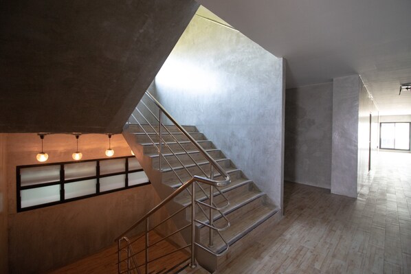 A modern interior with a staircase, wooden flooring, and a wall-mounted light fixture. - Rabbit Hotel Phimai (Phimai)