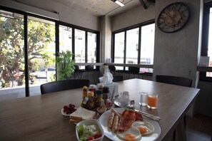 A breakfast table with various food items, a clock, and a view of the outside through large windows.