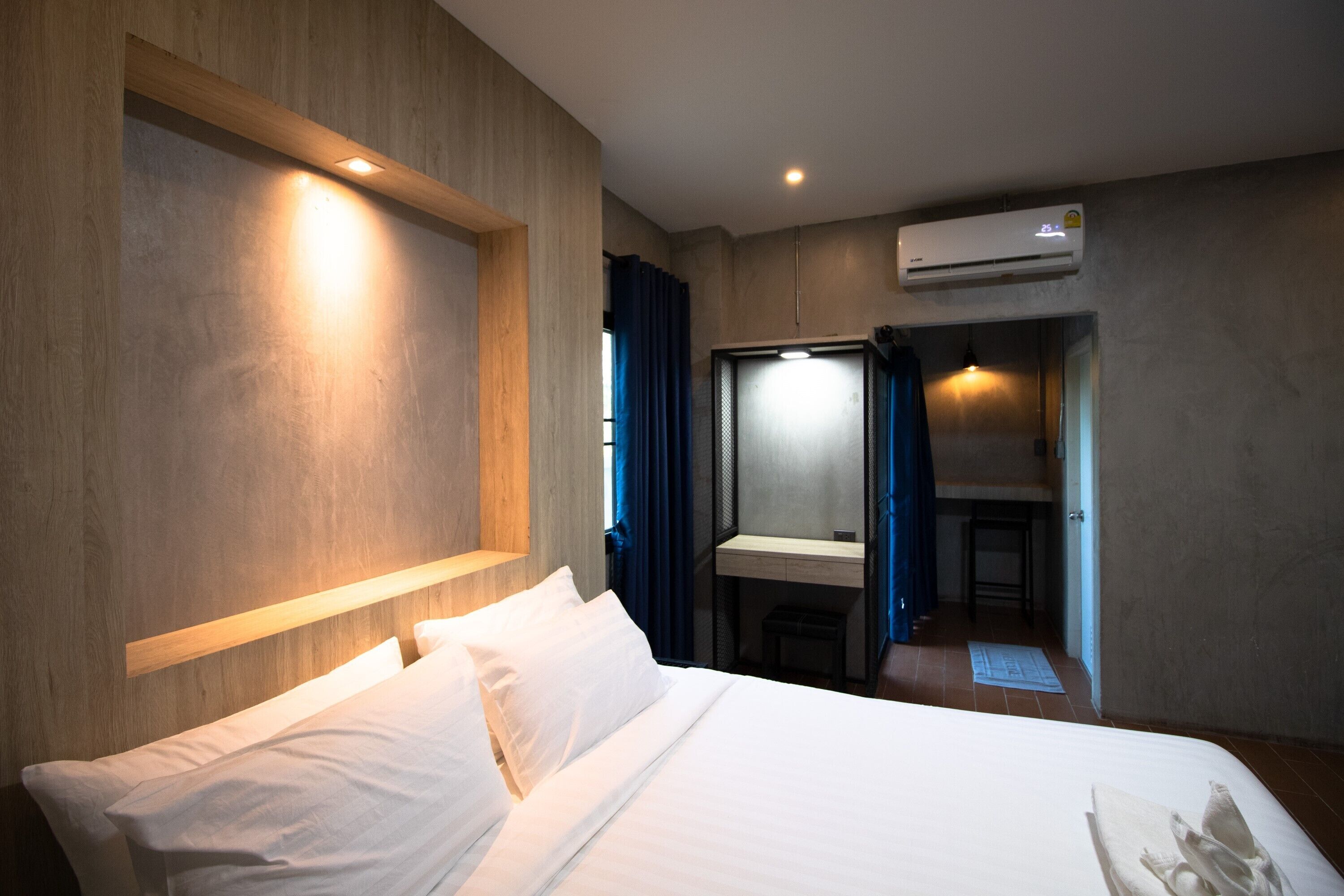 A hotel room with a bed, a desk, and an air conditioning unit.