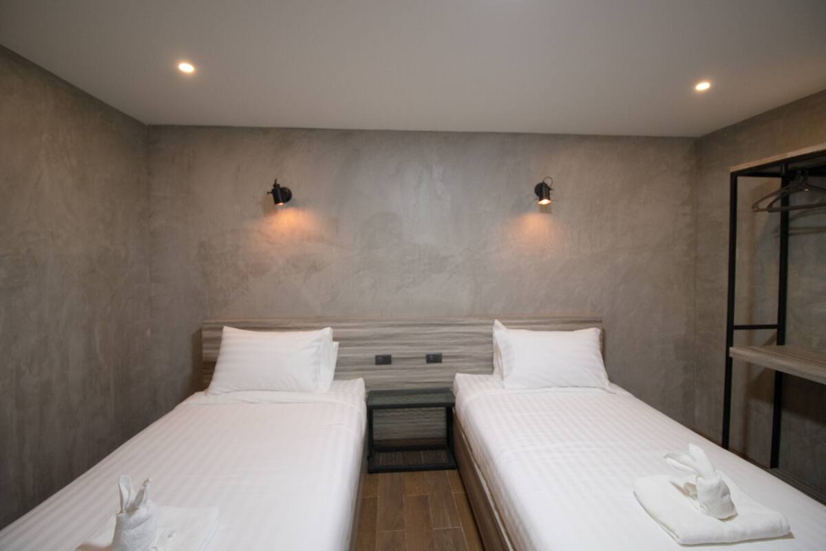 Habitación de hotel con dos camas, cabecera de madera y una mesita con una toalla.