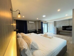 A hotel room with a large bed, a desk with a flat-screen TV, a chair, and a small kitchenette.