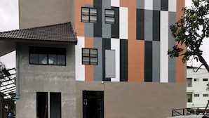 A swimming pool with a tiled floor, a building with a checkered facade, and a tree in the background. - Rabbit Hotel Phimai (Phimai)