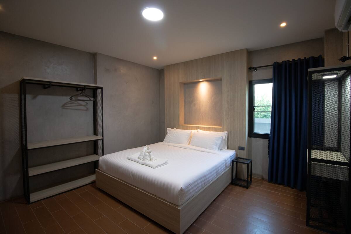 Un dormitorio moderno con una cama grande, un armario con estantes, una mesita de noche y una ventana con cortinas.