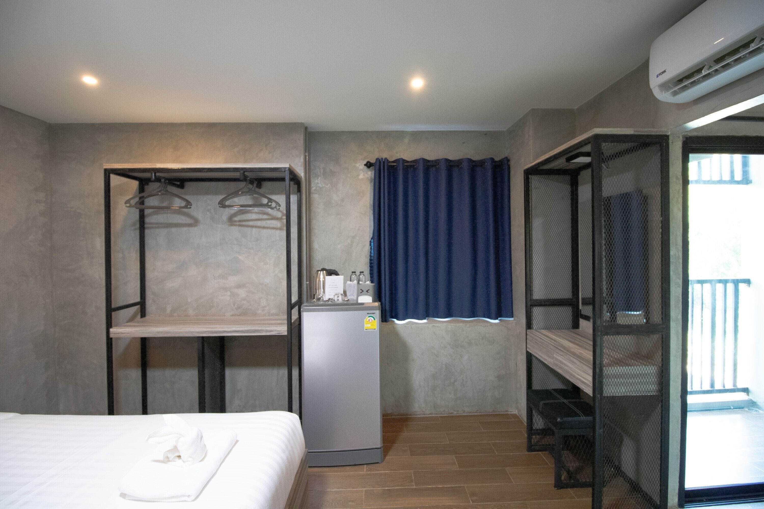 Habitación de hotel compacta con cama, kitchenette pequeña, zona de estar y balcón con barandilla.