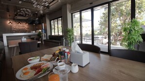 A breakfast table with eggs, bacon, toast, and juice in a modern hotel room with large windows and a view of the outdoors. - Rabbit Hotel Phimai (Phimai)