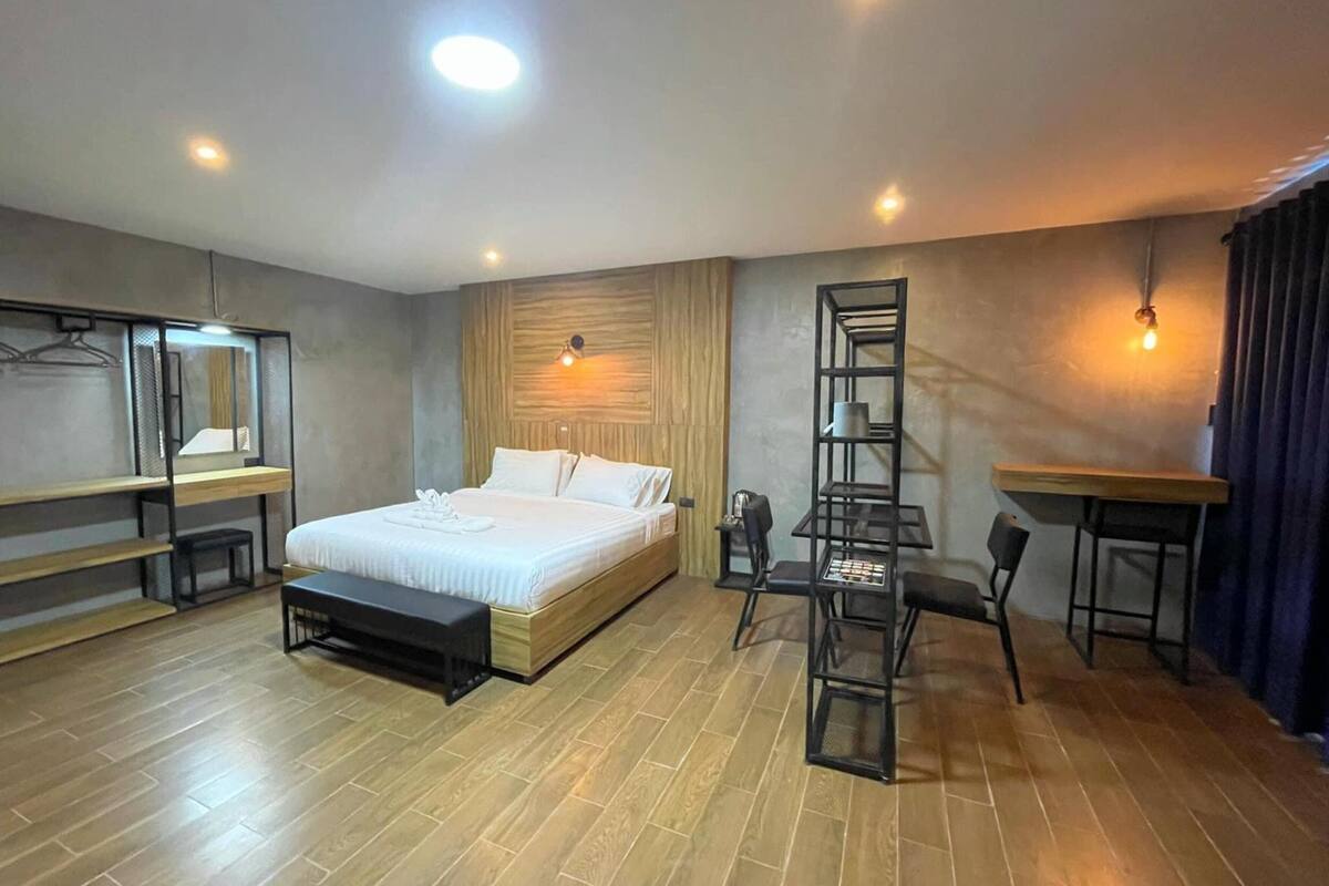 Habitación de hotel moderna con piso de madera, cama con ropa blanca, escritorio con silla y una estantería.