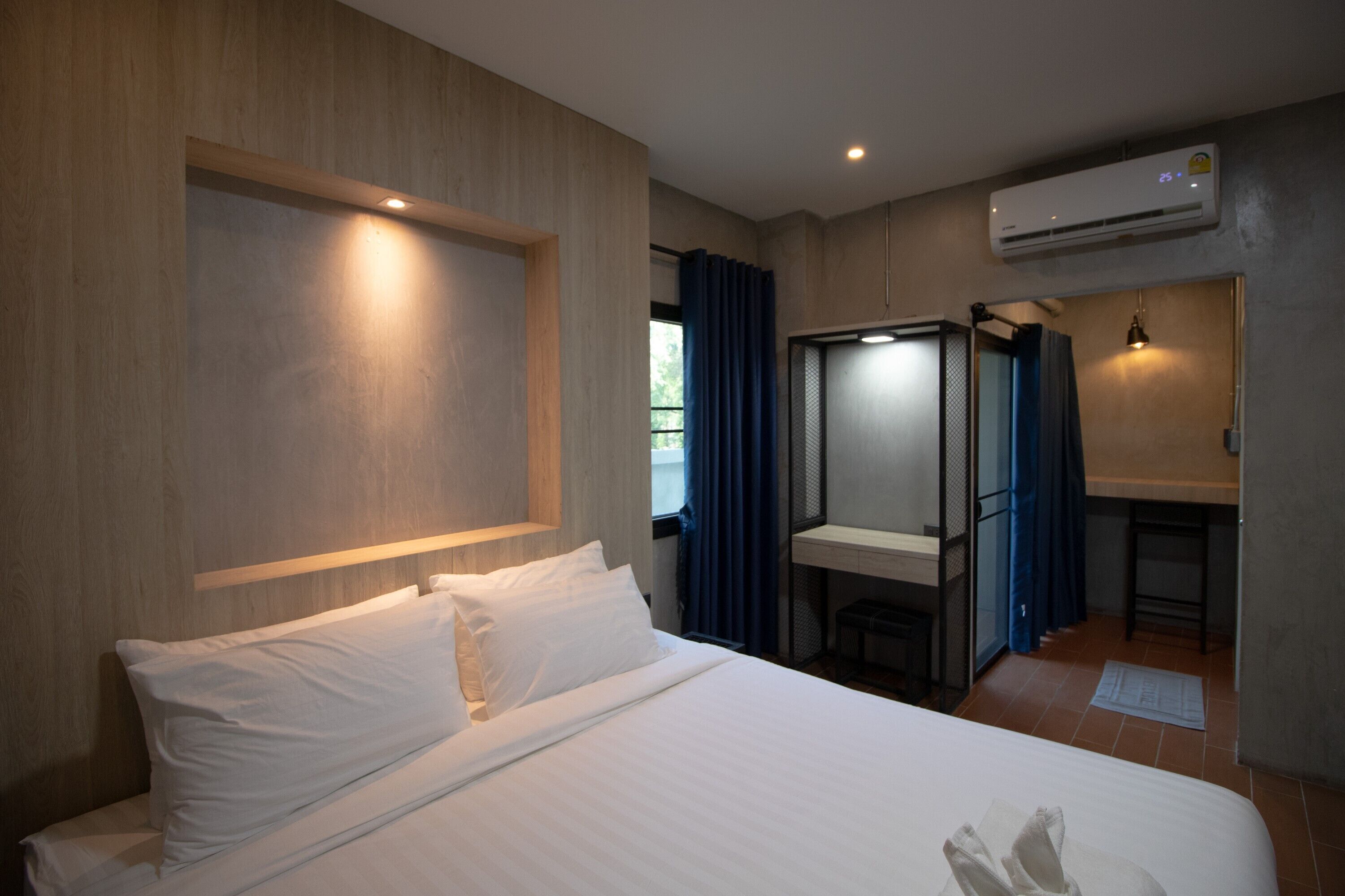 A hotel room with a bed, a desk, and an air conditioning unit.