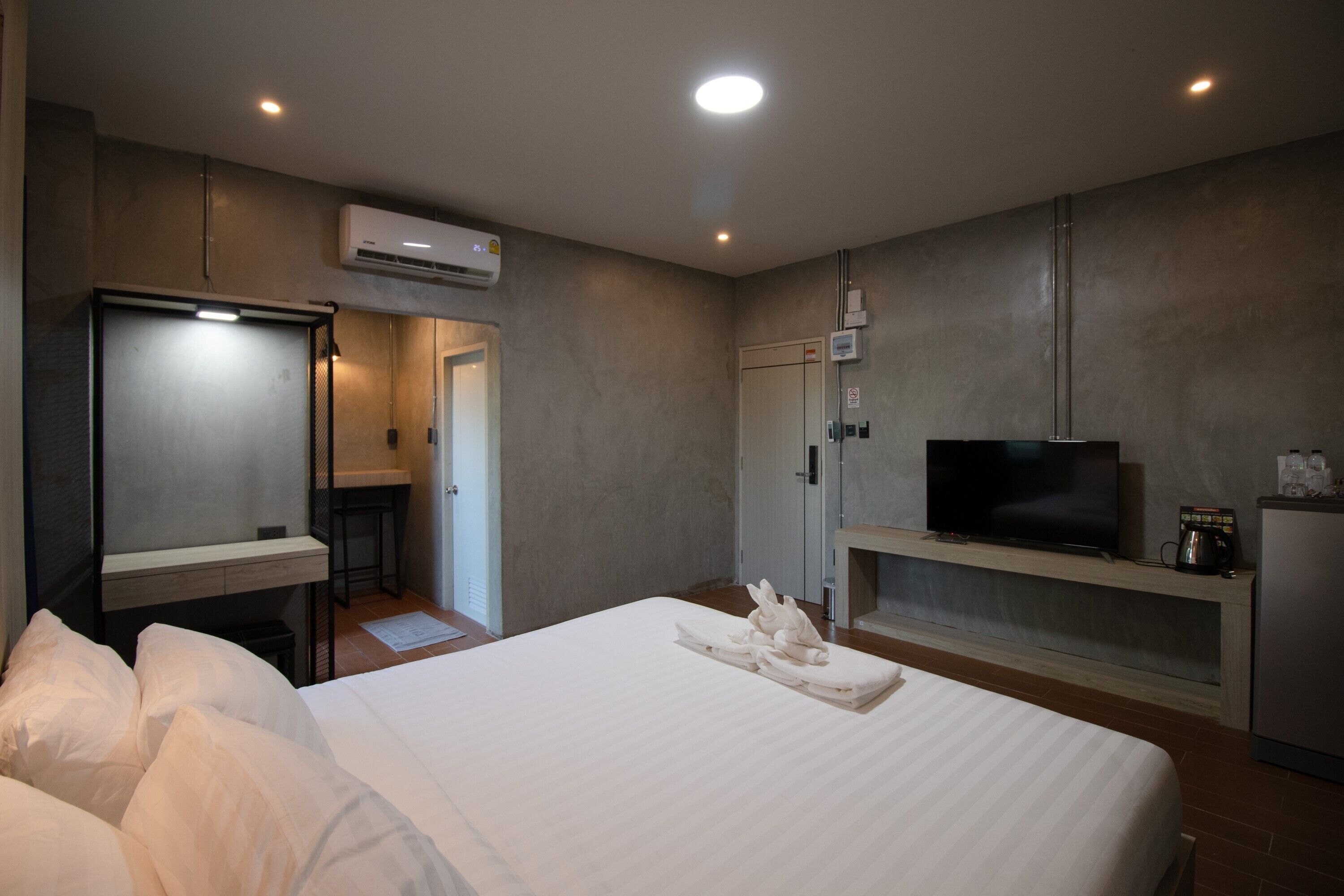 A hotel room with a bed, a TV, a minibar, and a desk with a chair.