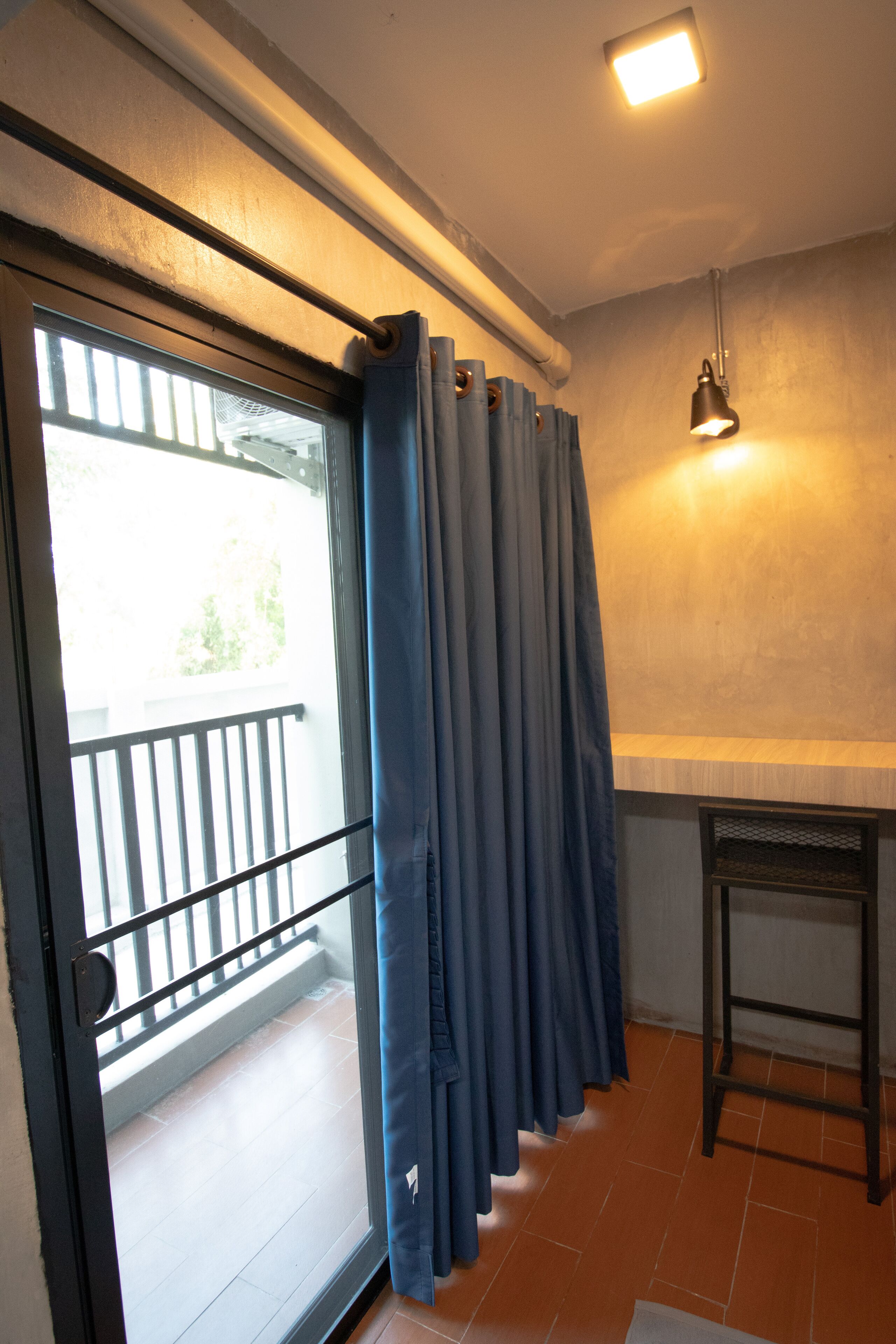 A room with a sliding glass door leading to a balcony, a dark-colored table, and a hanging light fixture.