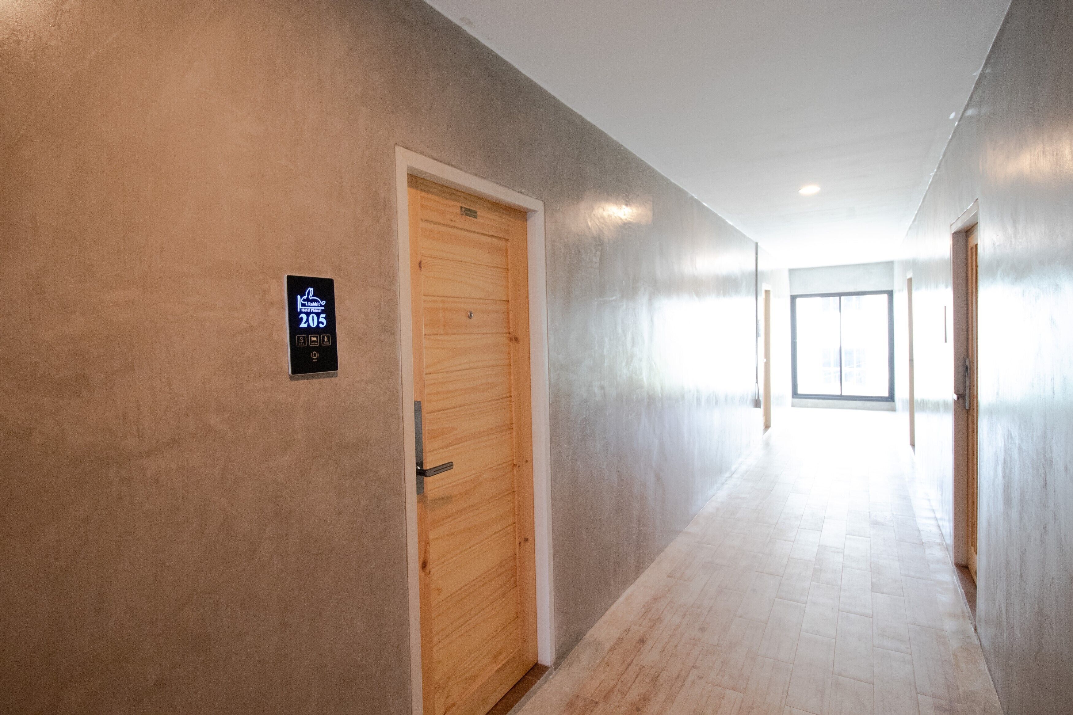 Un pasillo con una puerta de madera con el letrero "205" y un anuncio que indica la marca "Kohler".