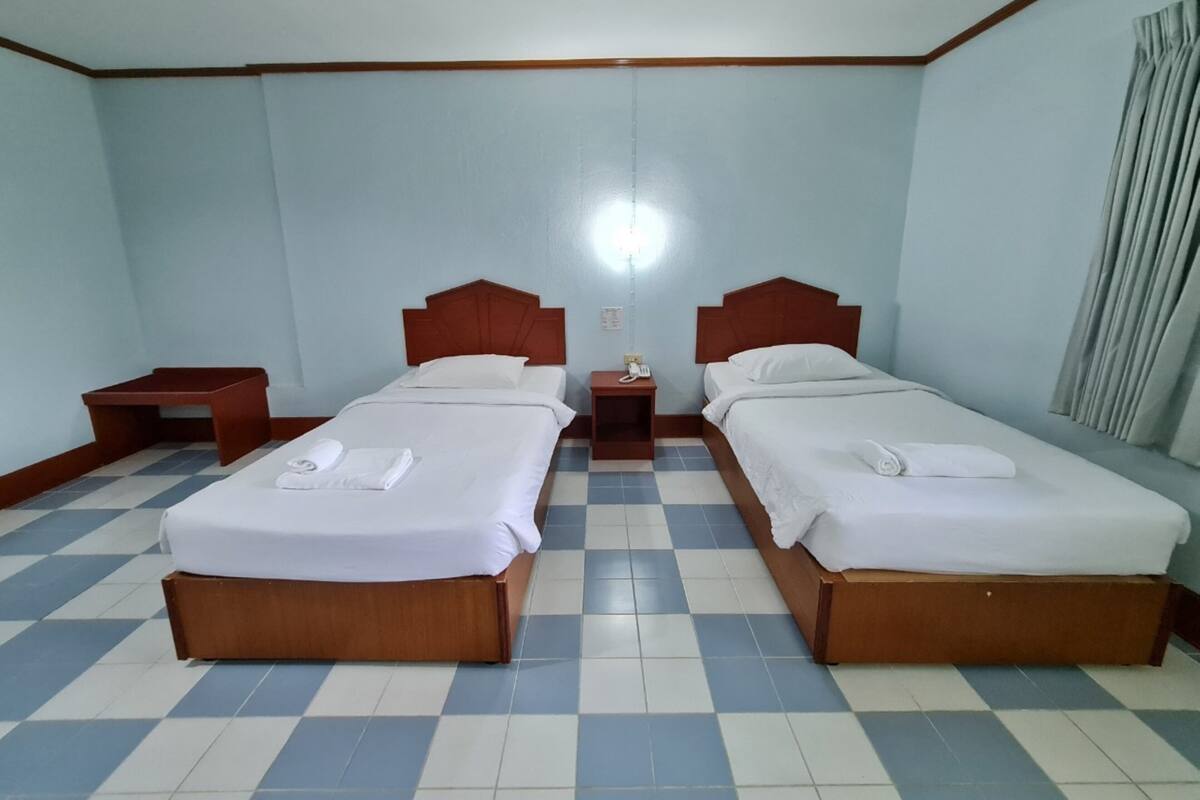 Une chambre d’hôtel avec deux lits, une table de chevet, une lampe et une fenêtre avec des rideaux.