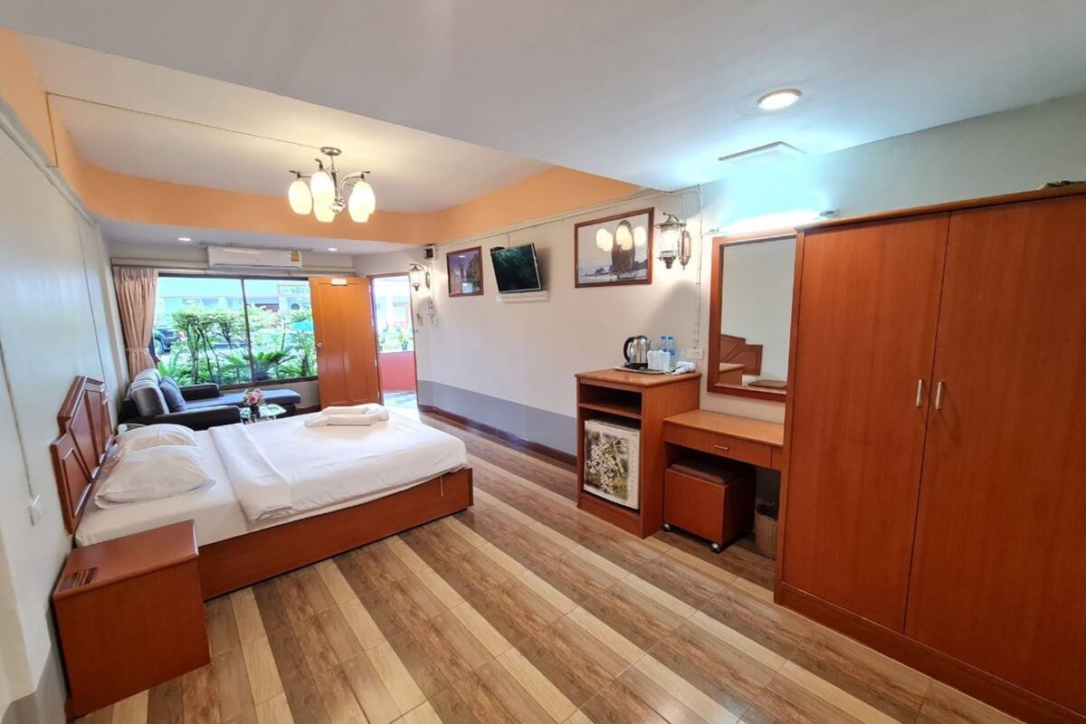 Une chambre d’hôtel avec un lit, une armoire en bois, un bureau avec un miroir et une fenêtre donnant sur un paysage verdoyant.