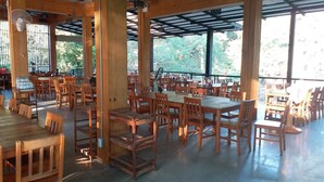 A spacious indoor dining area with wooden tables and chairs, large windows, and ceiling fans. - Saney Apartment (Pak Chong)