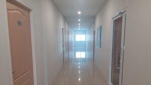 A hallway with a polished floor, doors on both sides, and a bright window at the end. - Saney Apartment (Pak Chong)
