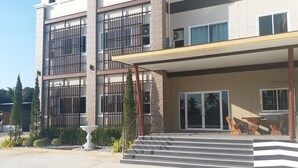 A multi-story hotel with a covered entrance, outdoor seating, and a staircase leading to the entrance. - Saney Apartment (Pak Chong)