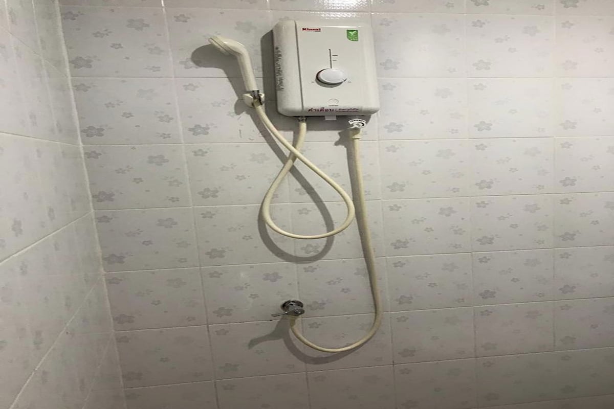 A bathroom with a wall-mounted shower unit, a control knob, and a handheld showerhead.