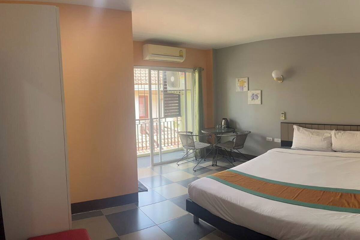 A hotel room with a bed, a small table with chairs, a balcony with a view, and an air conditioning unit.