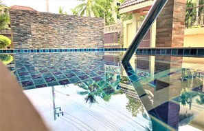 Une piscine avec un mur en pierre et un bord carrelé, entourée de bâtiments et de palmiers.