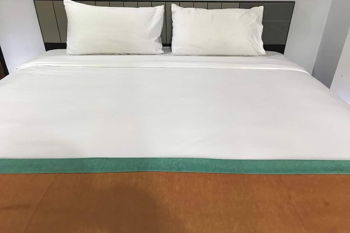 Una cama con ropa blanca y un detalle verde al pie.