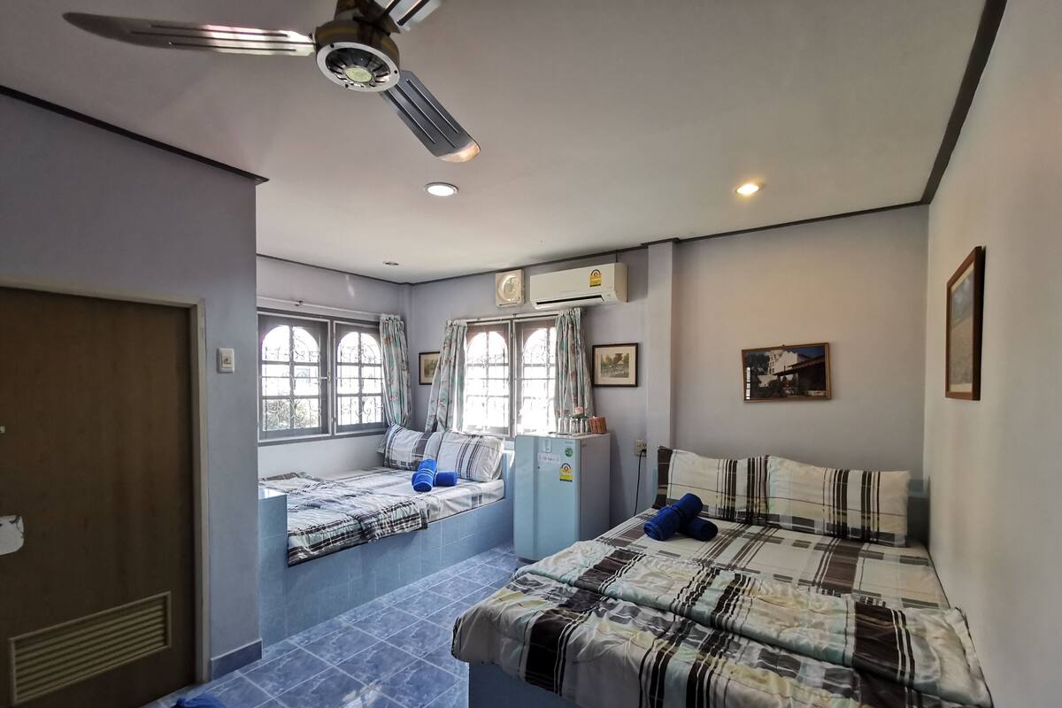 A bedroom with a bed, a ceiling fan, an air conditioning unit, and a window with curtains.