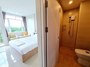A hotel room with a bed, a window with curtains, a bathroom with a shower, and a toilet. - Studio309@Phuket (Phuket)