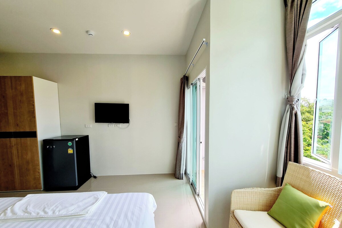 Een hotelkamer met een bed, een aan de muur bevestigde televisie, een klein bureau en een raam met gordijnen.