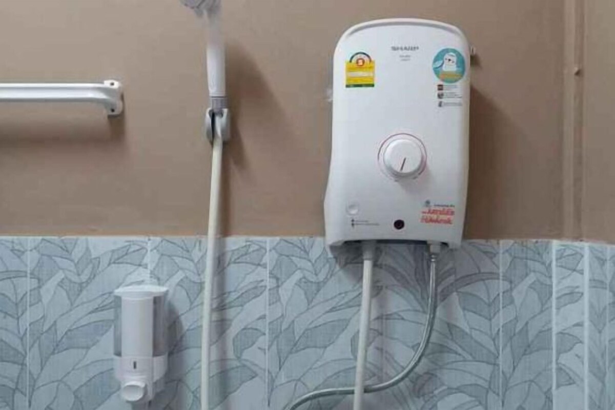 Calentador de agua instalado en una pared, con una perilla de control, un grifo y una toma de corriente debajo.