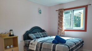 Ein Schlafzimmer mit einem Bett, einem Nachttisch mit Wasserkocher, einer kleinen Ablage für Tassen und einem Fenster mit Vorhängen.