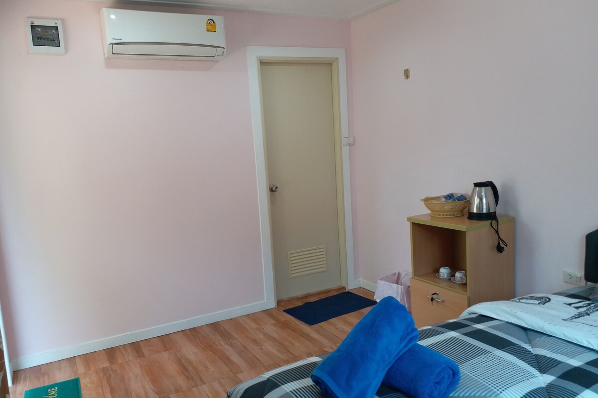Une chambre d’hôtel comprenant un lit, une table de chevet avec une bouilloire et un bol, une armoire, une porte et un appareil de climatisation.