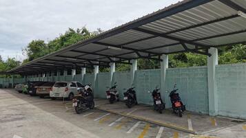 A covered parking area with several motorcycles and cars parked under a metal roof.