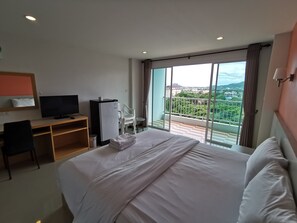 Een hotelkamer met een bed, een bureau met een televisie, een koelkast en een balkon met uitzicht op de stad.