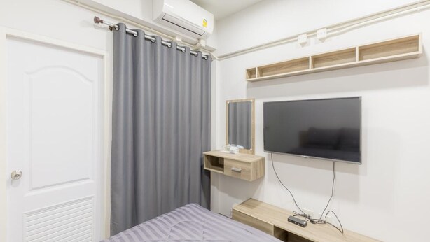 A bedroom with a bed, a TV, a mirror, and a small wooden shelf. - MiddleWay House (Bangkok)