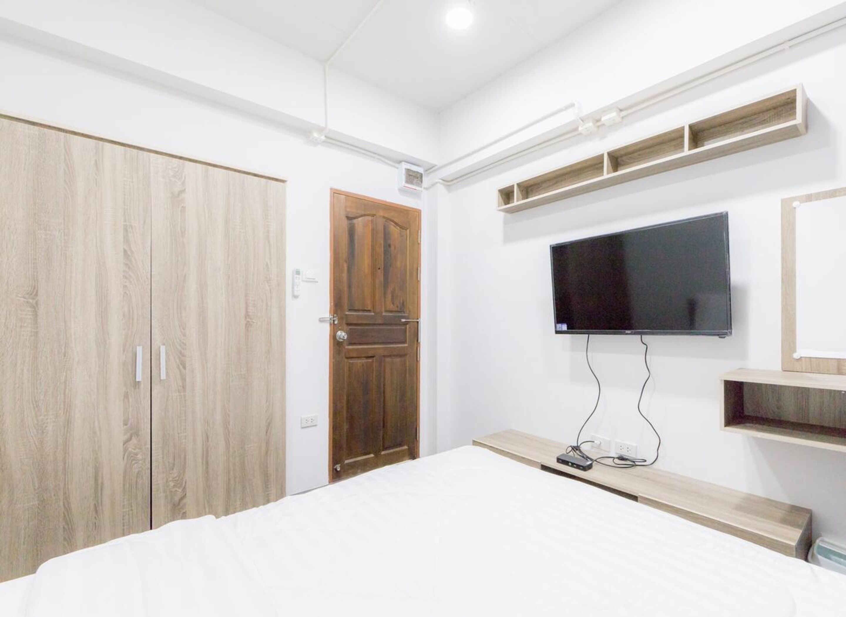 A bedroom with a large bed, a wardrobe, a television mounted on the wall, and built-in shelves.