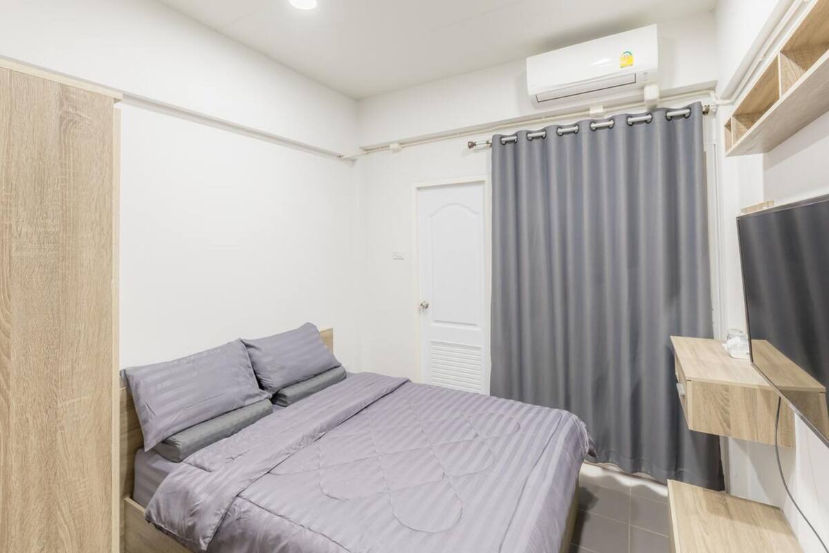 A modern bedroom with a bed, grey curtains, a white door, and a built-in TV shelf.