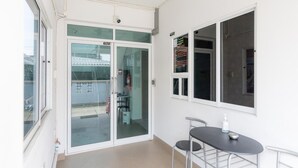 A balcony with a glass door, a small table with two chairs, and a ceiling fan. - MiddleWay House (Bangkok)