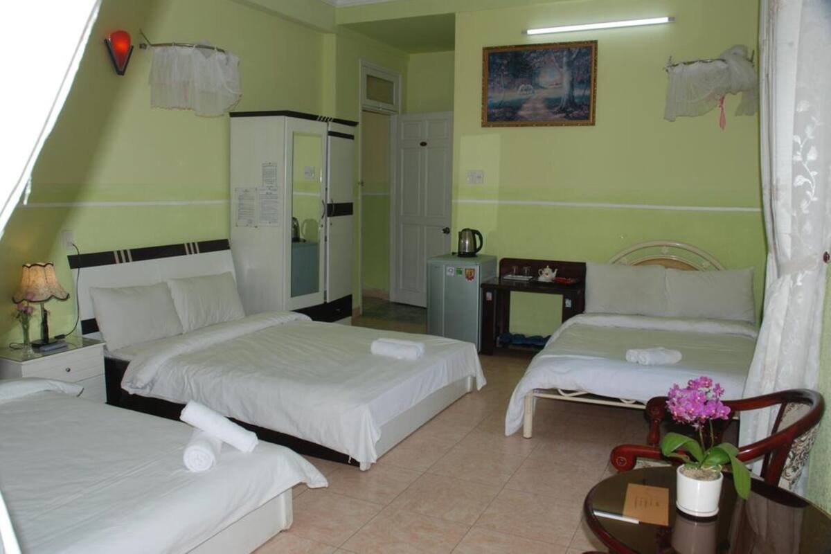A hotel room with two beds, a desk, a chair, a small table with a plant, and a painting on the wall.