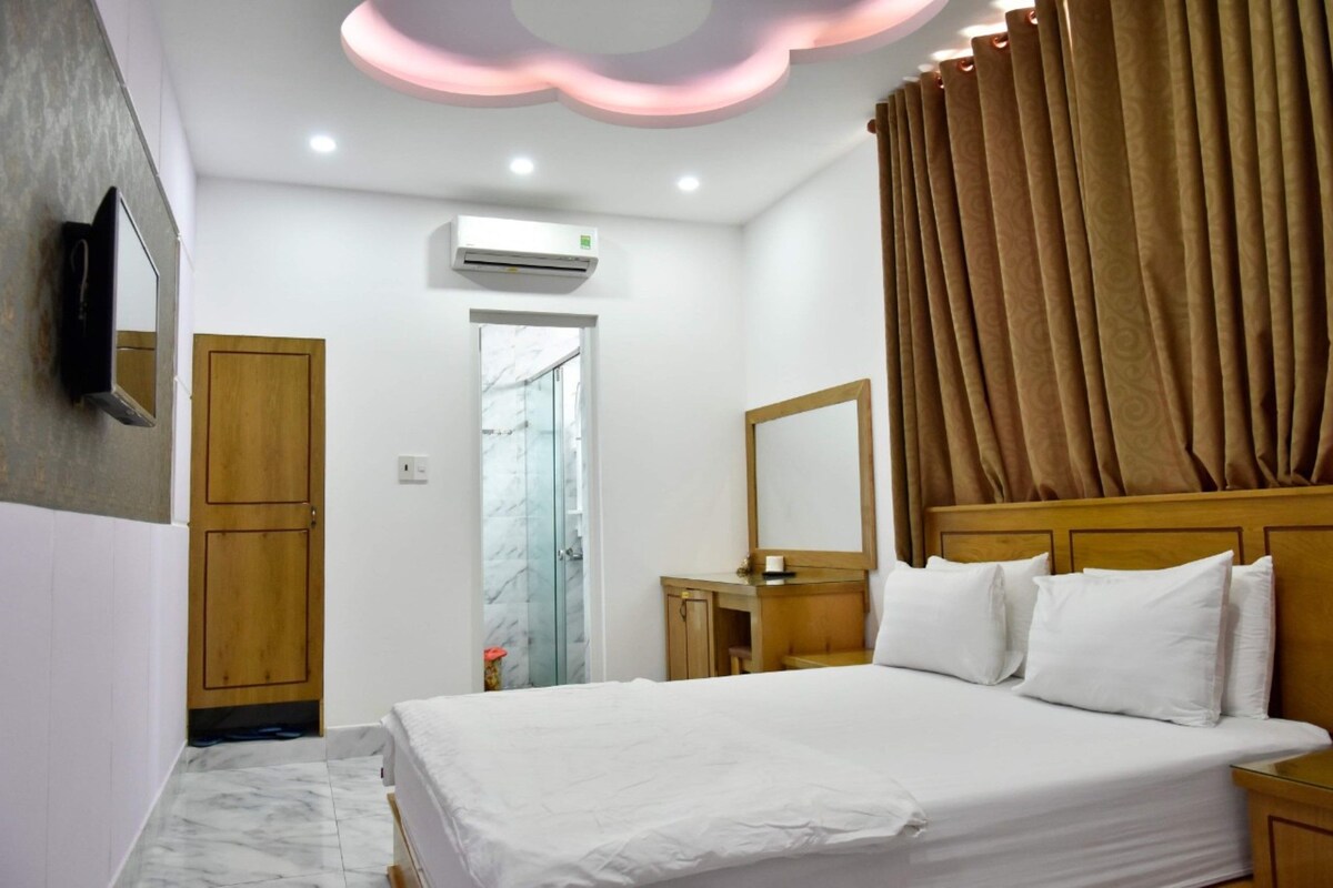 A hotel room with a bed, a wooden headboard, a mirror, a bedside table, and a shower area.