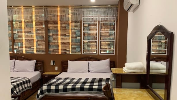 A bedroom with two beds, a wooden dresser, a mirror, and a window with a view of a brick wall. - Hoang Yen Nhi Hotel (Ho Chi Minh City)
