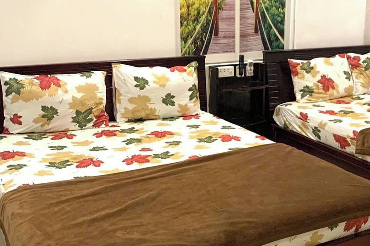A hotel room with two beds, each with floral bedding and a brown blanket. There is a window with a view of a bridge and palm trees.