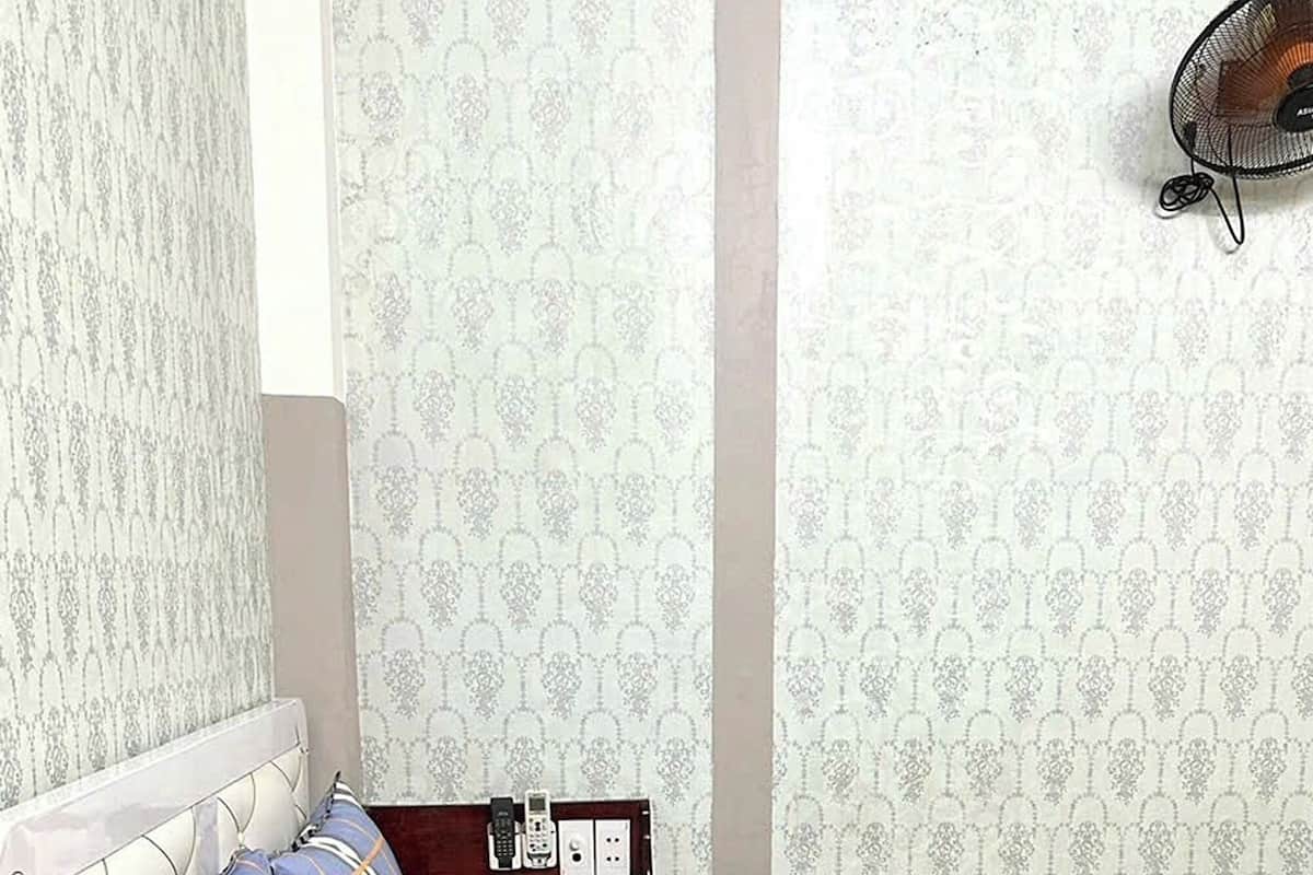 A neatly made bed with a plaid bedspread, a headboard, and a bedside table with a phone and a lamp.