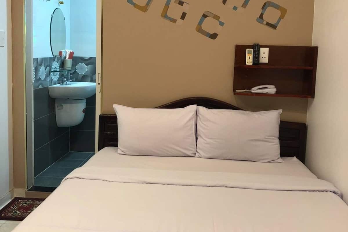 A hotel room with a bed, a bathroom with a sink and mirror, and an air conditioning unit on the wall.