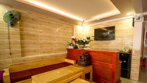A modern living room with a wooden bench, a glass-top table, and a TV mounted on the wall. - Phuc Dang Huy Hotel (Xuan Huong - Da Lat)
